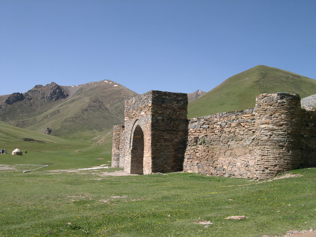 Oude stenen poort en muur in berglandschap langs de Zijderoute tijdens een groepsrondreis.