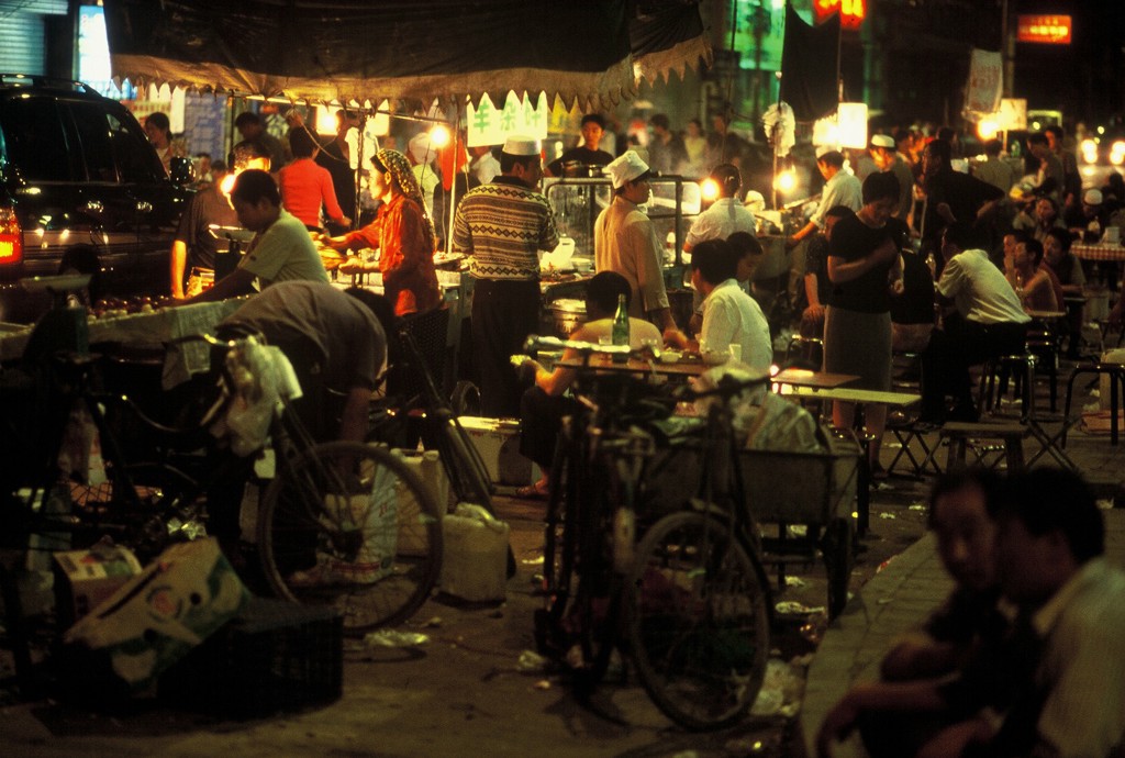 Drukke avondmarkt met eetkraampjes en zitplaatsen in China, verlicht door lampen.