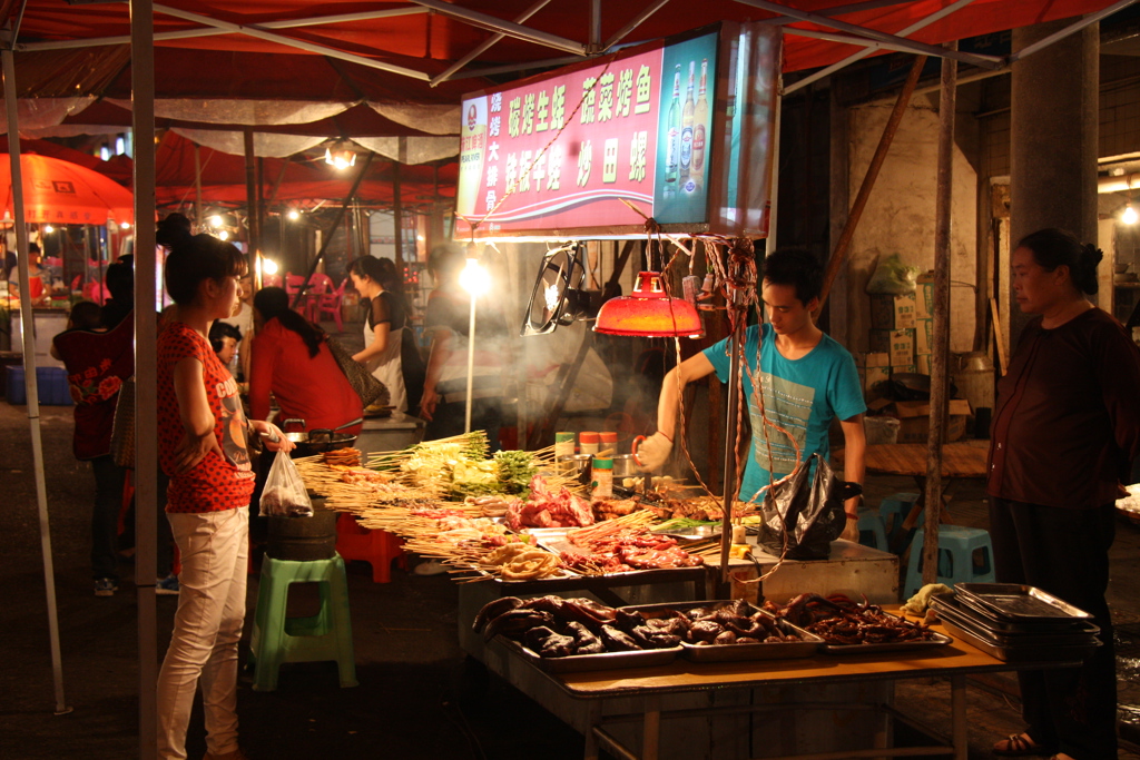Straatkraam met gegrilde spiesjes en groenten op een avondmarkt in China.