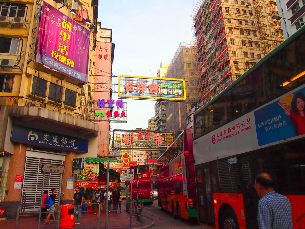 Drukke straat in Hongkong met neonreclames en dubbeldekkerbussen.