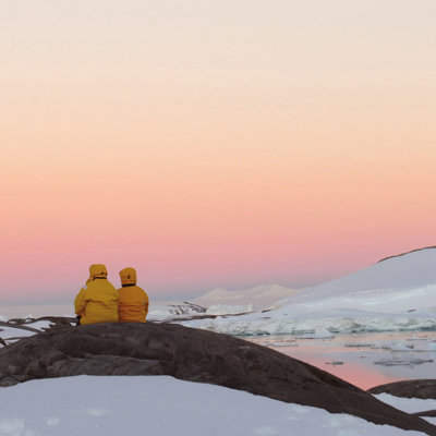 Reizigers in gele jassen kijken uit over het Antarctische ijslandschap bij zonsondergang tijdens de groepsrondreis.