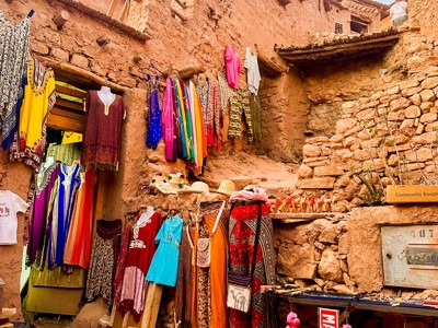Kleurrijke kleding en souvenirs in een straatmarkt tussen lemen huizen in Marokko.