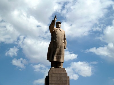 Monumentaal standbeeld van Mao Zedong tegen een blauwe lucht met wolken, langs de Route Zijderoute.