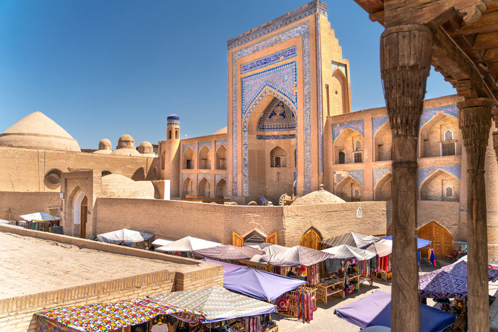 Historische madrassa met blauw tegelwerk en marktstalletjes langs de Zijderoute tijdens een groepsrondreis.