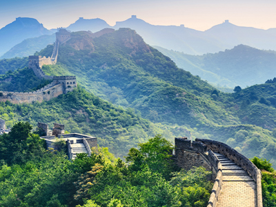 De Chinese Muur slingert over groene bergkammen bij zonsopgang.