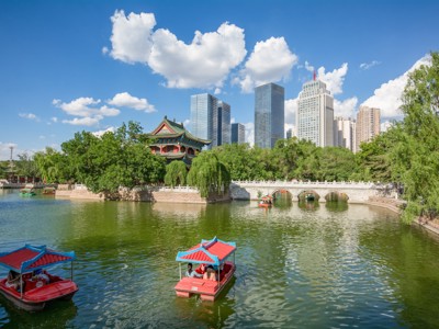 Bootjes op het meer in Beihai Park met traditionele paviljoens en skyline van Beijing op de achtergrond.