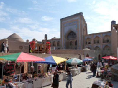 Markt met kleurrijke kraampjes voor een historisch madrasa-complex langs de Route Zijderoute.