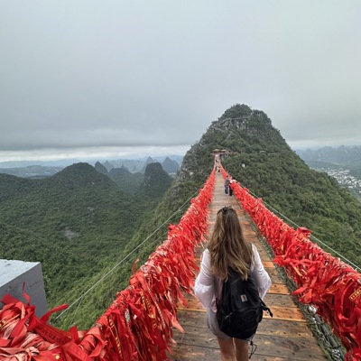 Wandelaar op hangbrug met rode linten boven groene karstbergen in China.