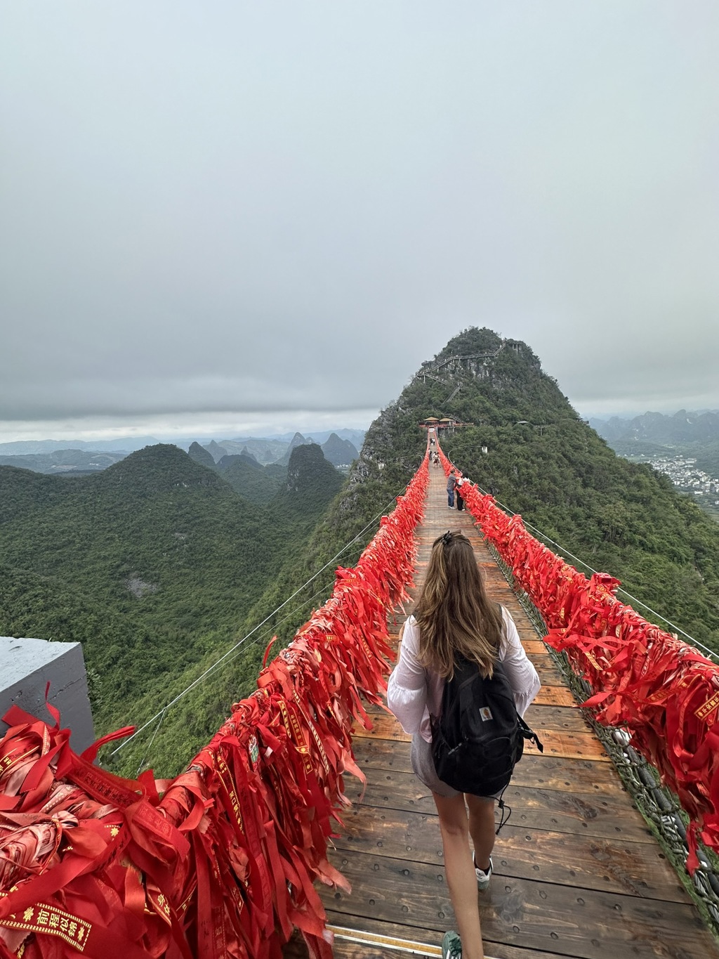Wandelaar op hangbrug met rode linten boven groene karstbergen in China.