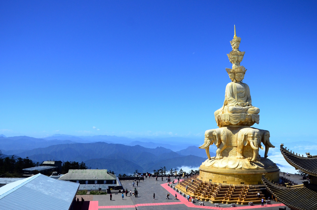 Gouden Boeddhabeeld op bergtop met uitzicht over berglandschap en tempeldak in China.