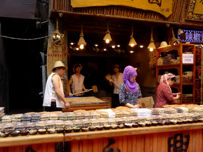 Kruiden- en snackkraam op een Chinese markt met verkopers en schalen vol gedroogde producten.
