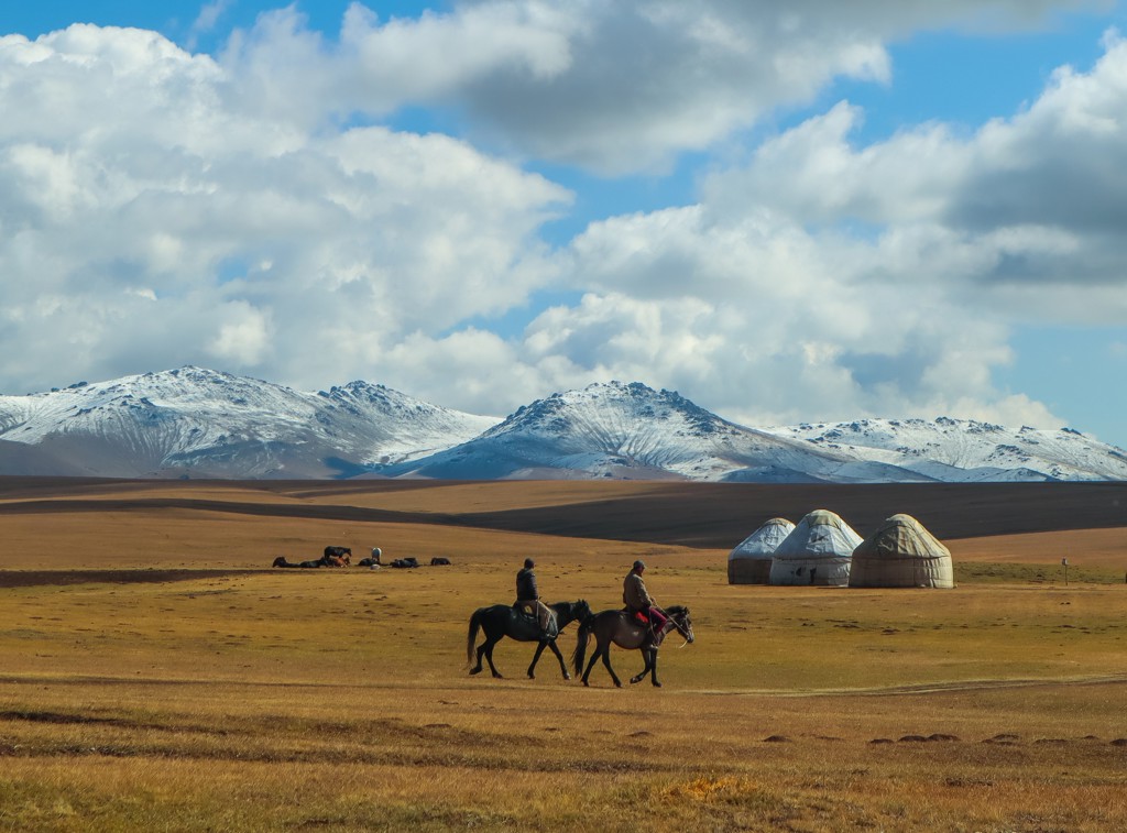 Ruiters te paard bij yurts in de steppe met besneeuwde bergen, tijdens groepsrondreis Zijderoute.