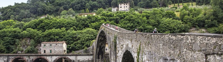 Fietsers op een historische stenen boogbrug over een rivier in Toscane, Italië.