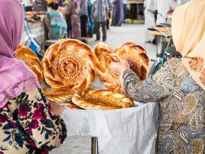 Vrouwen kopen vers gebakken, ronde broden op een markt langs de Route Zijderoute.