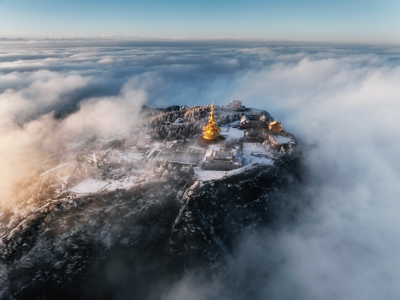 Gouden tempelcomplex op een besneeuwde bergtop, omringd door wolken en mist in China.